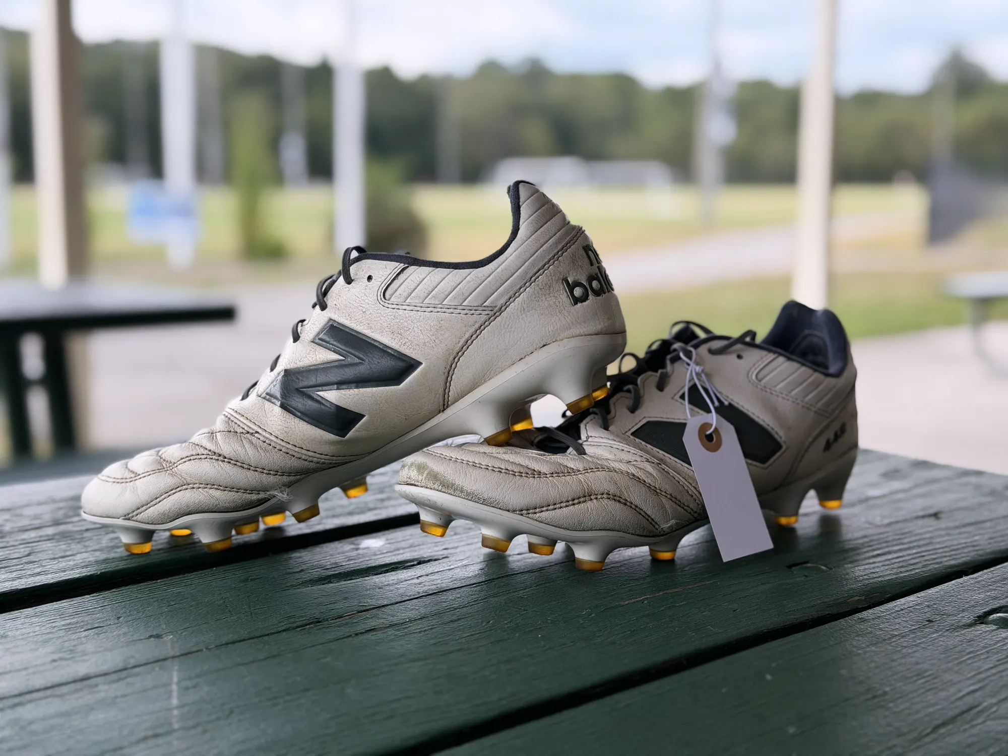 A cleaned pair of tan leather cleats on a picnic table with a handwritten size tag tied to the laces