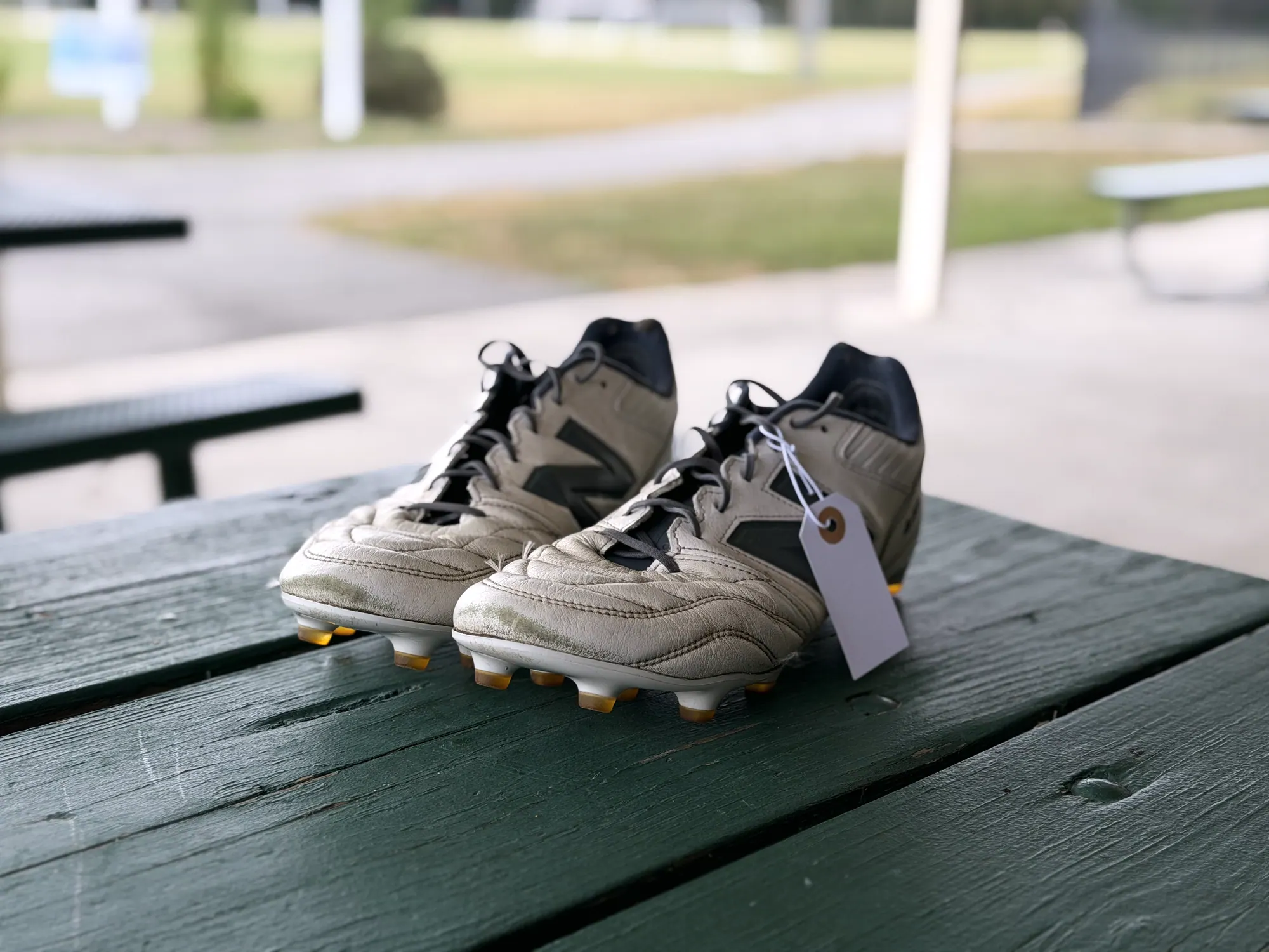 A cleaned, tagged pair of cleats resting on a picnic table beside the field